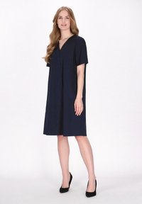 Dunkelblaues Kurzarmkleid mit V-Ausschnitt, lässiger Passform, knielang und glatter Textur, kombiniert mit schwarzen High-Heels.