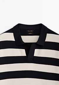 Polo shirt à rayures bleu marine et crème avec un tissu texturé, présentant un col court et une patte de boutonnage à trois boutons. Étiquette visible à l'intérieur.