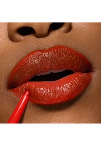 Pencil labbra rosso applicato su labbra lucide e piene, con una finitura liscia e vibrante. Il tono della pelle è caldo, offrendo un contrasto con il colore delle labbra.
