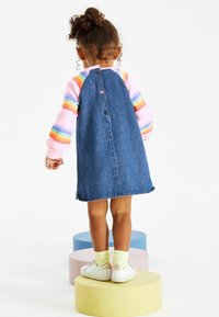 Denim jurk met een uitlopende vorm, voorzien van een knoopsluiting aan de achterkant. Gepaard met een roze gestreepte lange mouw shirt en witte sneakers.