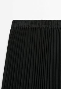 Jupe plissée noire avec taille élastique, présentée à plat sur un fond blanc.
