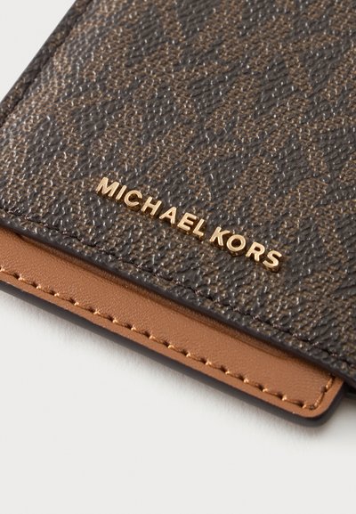 Крупен план на ъгъла на кафяво текстурирано кожено портмоне със златисто лого Michael Kors и кожена лайсна в цвят тен със шевове.