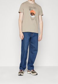 Beige bomulds-T-shirt med NASA-grafik; blå denimjeans; flerfarvede sneakers med stof- og gummidetaljer.