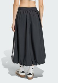 Čierna sukňa po kolená so zúženým pásom, s bielymi bočnými prúžkami. Hladká textúra, navrhnutá v voľnom, balónikovom tvare.