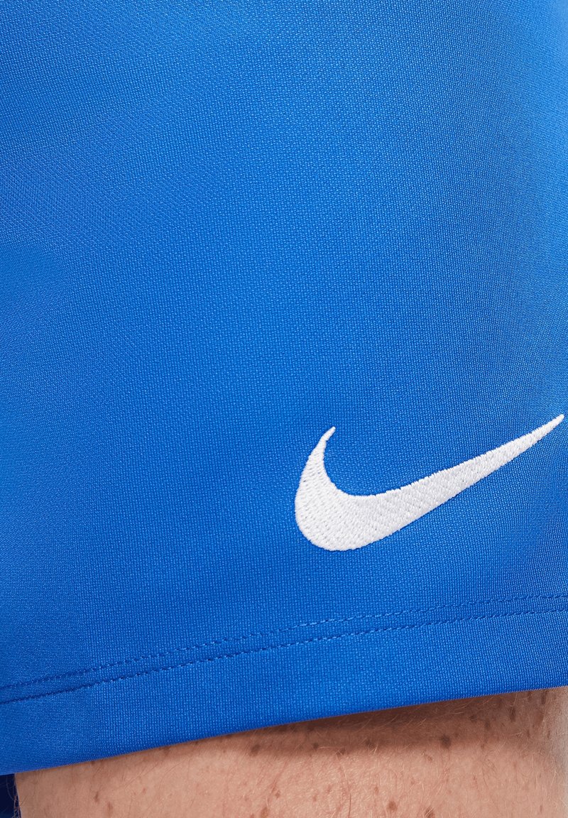 Gros plan sur un tissu bleu avec le logo Nike swoosh blanc brodé sur la peau d'une personne avec des taches de rousseur claires.