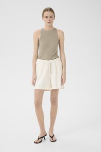 Beige ribbet tank top med rund hals, kombinert med kremfargede elastiske shorts; modell iført svarte flip-flops, stående mot en hvit bakgrunn.