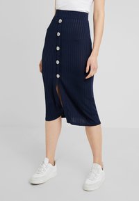 Mörkblå ribbad midijol med en framspalt och sex dekorativa knappar. Kombinerad med vita sneakers. Slät tygtextur och skräddarsydd passform.