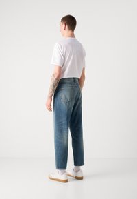 Világoskék denim farmer, laza szabással, öt zsebes kialakítással. Egy sima fehér pólóval és fehér edzőcipővel párosítva.