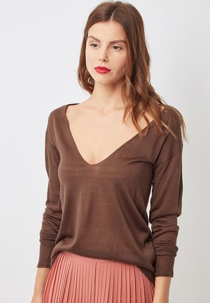 Suéter marrón de manga larga con un diseño de escote en V profundo y textura suave, combinado con una falda rosa plisada.