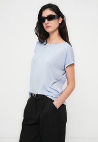 Ανοιχτό μπλε κοντομάνικο τοπ από απαλό ύφασμα, στιλιζαρισμένο με μαύρο παντελόνι ψηλόμεσο, με ομαλή υφή και άνετη εφαρμογή.