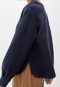 Sweat-shirt bleu marine avec manches longues bouffantes, encolure arrondie et fentes latérales à l'ourlet. Texture douce, coupe décontractée.