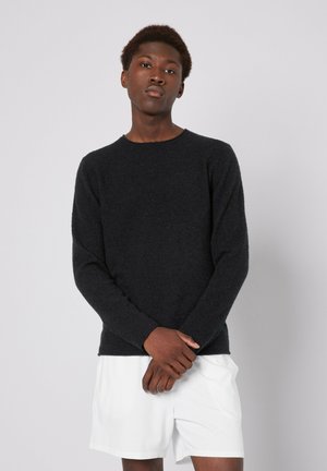 Dark gray knitted sweater with long sleeves and a round neckline. Soft texture and slim fit, paired with white shorts. Minimalist design.