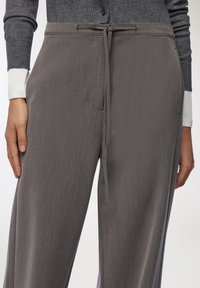 Szare spodnie o szerokich nogawkach z teksturowanej tkaniny, z elastycznym paskiem i bocznymi kieszeniami. Tkanina ma delikatne pionowe paski.