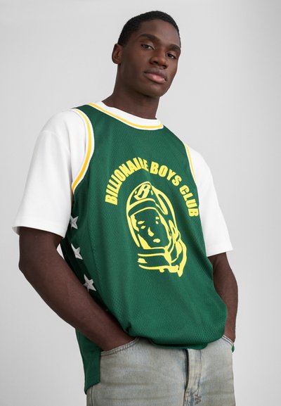 Tricou din plasă verde cu accente galbene, prezentând textul "Billionaire Boys Club" și un grafic cu un astronaut. Purtați cu o cămașă albă dedesubt.