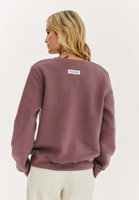 Zakurzona mauve bluza z prążkowanym kołnierzem, luźnym krojem i naszywką na plecach. Miękka bawełniana mieszanka o gładkiej fakturze.