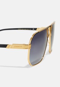Ochelari Carrera cu ramă din metal auriu, formă rectangulară, lentile cu un gradient închis și accente din cauciuc negru pe brate.