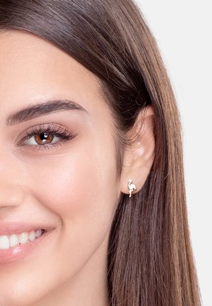 Sølv flamingo stud ørering med en glat overflade og minimalistisk design, båret i venstre øre af en person med langt, glat hår.
