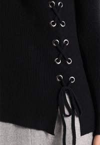 Musta ribbineulottu neulepaita, jossa hopeiset silmukat ja sivulla ristitetyönyöritys. Hihansuun reunassa solmittava koriste.