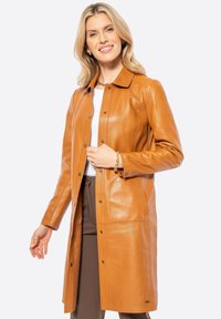 Bruine leren jas met een gekraagde halslijn, drukknoopsluiting en zijzakken. Gladde textuur, knielange stijl en een getailleerde pasvorm.