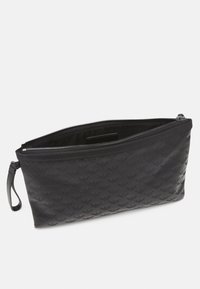 Svart läderclutch med pr präglat repetitivt mönster av örnlogotyper, dragkedjestängning och handledsrem på en vit bakgrund.