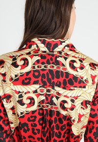 Rød og sort leopardprint skjorte med gyldne barok-stil mønstre, klassisk krave og detaljerede accenter henover ryggen.