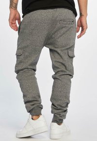 Grey sweatpants with a textured fabric, tapered fit, and side cargo pockets. Worn with white sneakers.