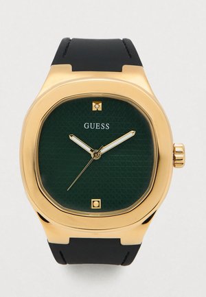 Orologio da polso Guess tono oro con quadrante verde scuro testurizzato, lancette bianche e dorate, indicatori delle ore minimali e cinturino in pelle nera.