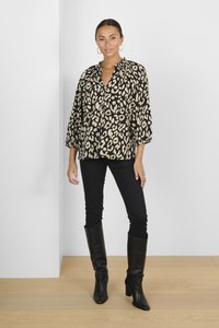 Blusa leopardata nera e beige con vestibilità rilassata, maniche a 3/4 e scollo arricciato, abbinata a jeans skinny neri e stivali al ginocchio.