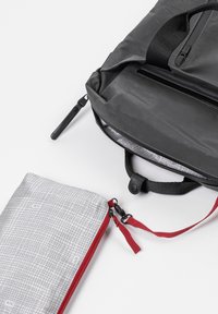 Zaino nero con texture, dotato di una tasca con zip, abbinato a un astuccio grigio a quadri con zip rossa e maniglia in tessuto per un facile accesso.