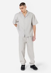 Camisa de manga curta cinza claro, com colarinho, fecho de botão e riscas verticais, combinada com calças a condizer. Sapatos pretos completam o visual.