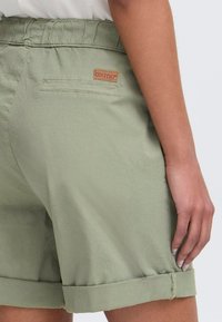 Grønne bomullsshorts med avslappet passform, elastisk midjebånd, rullede kanter og en baklomme med en liten brun logo-patch.