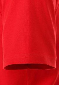 Rød bomulds-t-shirt med korte ærmer, der har en glat tekstur og ren syning langs sømmen. Ingen synlige mønstre eller designs.