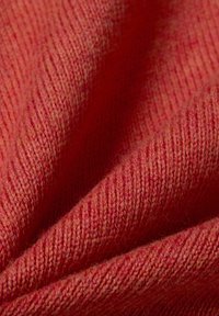 Strickstoff in verschiedenen Rottönen mit einer gerippten Textur und weichem, leicht flauschigem Finish mit subtilen Farbnuancen.