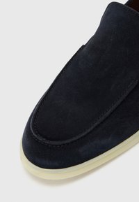 Marinblå mockaskor med rundad tå och sydda detaljer, med en ljus gummisula. Slät yta, minimalistisk design.