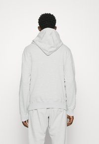 Sudadera con capucha de color gris claro, con bolsillo canguro, puños y dobladillo de canalé. Tela suave con un ajuste relajado. Combinada con pantalones de chándal a juego.