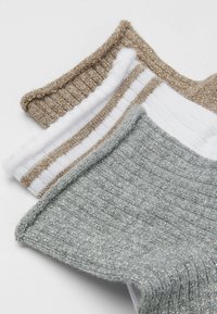 Tre paia di calzini a costine: uno beige con paillettes, uno bianco con strisce beige e uno grigio con fili argentati, tutti con polsini texturizzati.