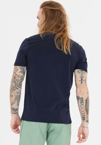 Navy sininen puuvillapaita lyhyillä hihoilla, pyöreällä kaula-aukolla ja rentolla istuvuudella, esitetty takaa, jossa on tatuoidut kädet.