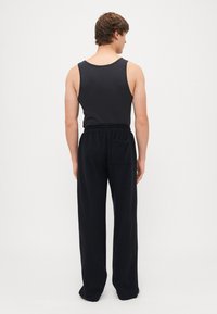 Schwarzes Tanktop und lockere schwarze Hose mit einem Kordelzugbund und Seitentasche. Schlichtes, entspanntes Design und weicher Stoff.