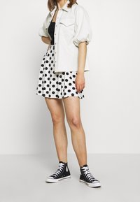 Chemise blanche surdimensionnée, débardeur noir, jupe noire à pois blancs, et baskets montantes noires avec lacets blancs.