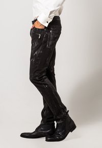 Jeans in denim nero con un motivo testurizzato e usurato e hardware in argento. Il design include una vestibilità slim e diverse tasche.