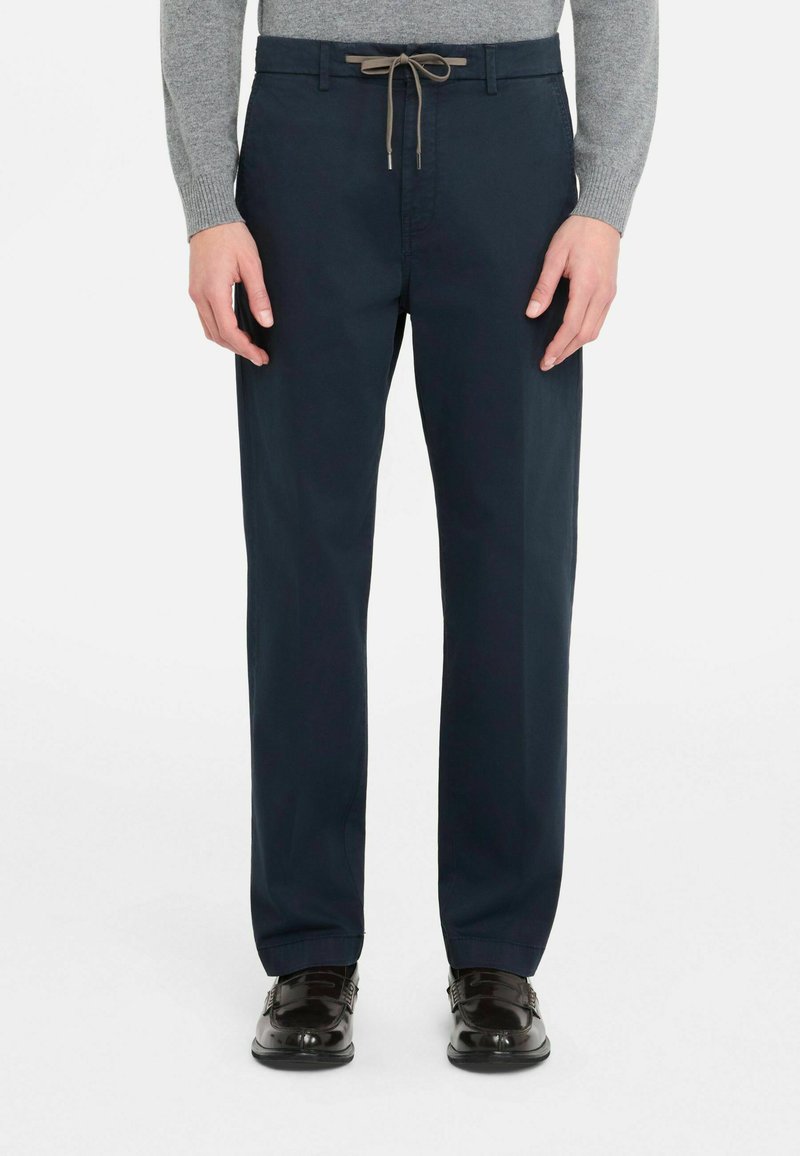 Pantalon en coton bleu marine avec une taille à cordon, coupe droite et une légère brillance, assorti à des chaussures noires.