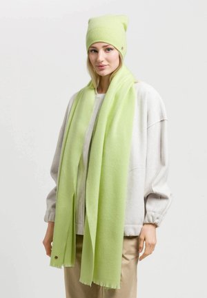 Green knitted beanie and matching scarf made of soft, lightweight fabric; beanie has a folded edge, scarf features raw edges.