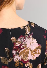 Blumenkleid mit schwarzem Hintergrund, großen rosa und burgunderfarbenen Blumen, einem runden Ausschnitt und einem diskreten Reißverschluss auf der Rückseite.