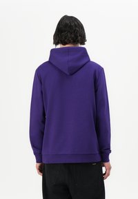 Sudadera morada con una capucha grande, mangas largas y puños acanalados. La tela parece suave y texturizada, con un diseño simple sin patrones.