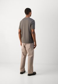 Grå kortärmad t-shirt med en avslappnad passform, i kombination med ljusbeiga byxor. Outfiten har en enkel design och mjuk textur.