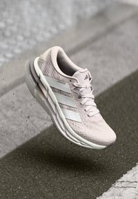 Lichtroze hardloopschoen met een gestructureerd bovenwerk, drie witte strepen, een dempende zool en het "ADISTAR" logo aan de zijkant.