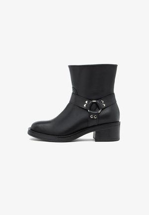Zwarte leren enkelboot met een lage blokhak, banddetail en zilveren metalen ring en klinknagels aan de zijkant.