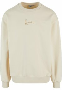 Kremfarget genser laget av mykt stoff. Har en ribbestrikket halslinning og mansjetter, med en subtil brodert logo i gull.