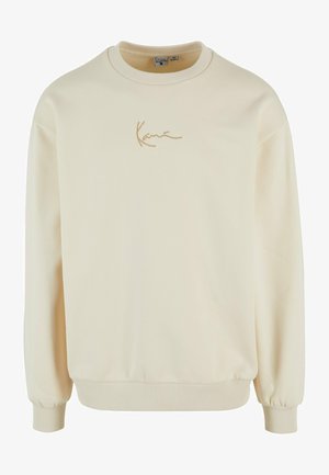 Krēmkrāsas sporta krekls, kas izgatavots no mīksta auduma. Tam ir ribota apkakle un aproces, kā arī diskrēts izšūtā zīme zeltā.