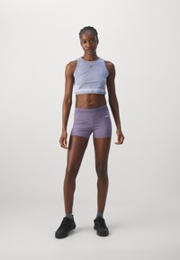 Vaaleanvioletti urheilu crop-top, jossa on Nike-logo, yhdistettynä samasta väristä istuviin lyhyisiin housuihin. Molemmat ovat valmistettu joustavasta ja sileästä materiaalista. Mustat lenkkarit.